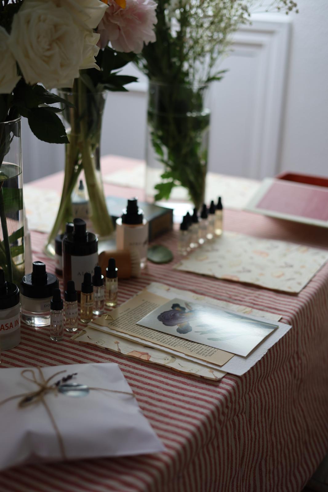 Mesa de taller con frascos de perfume, flores blancas y un paquete atado con cuerda